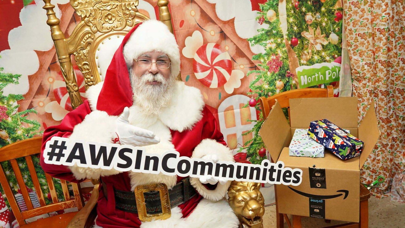 AWS in Communities: Santa Clause holding up a sign that reads '#AWSinCommunities'