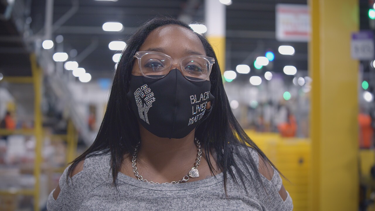 a Black woman who is an Amazon employee looks at the camera. She is wearing a face mask.