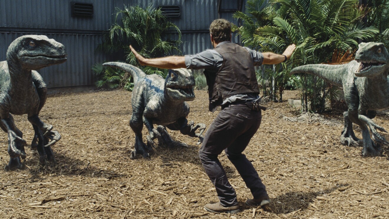 Man facing three velociraptors with arms outstretched in Jurassic World scene.