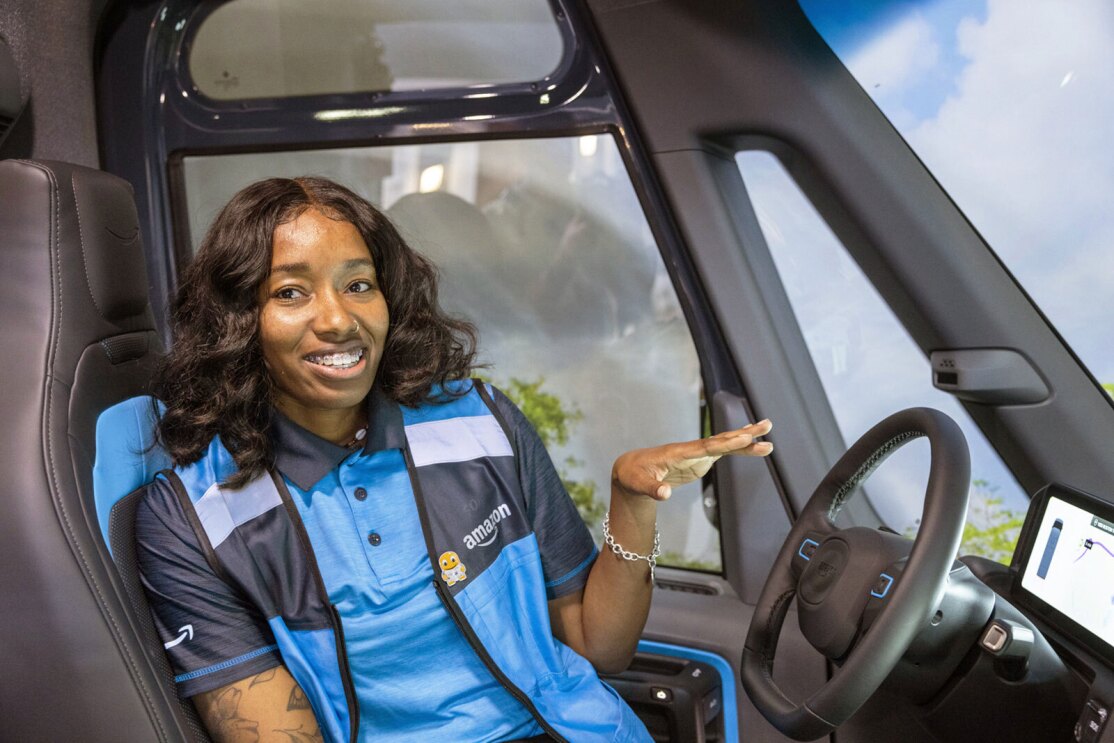 A photo of Brandi Monroe, a delivery driver for Kangaroo Direct, an Amazon Delivery Service Partner, sitting in the driver seat of an Amazon delivery van from Rivian.