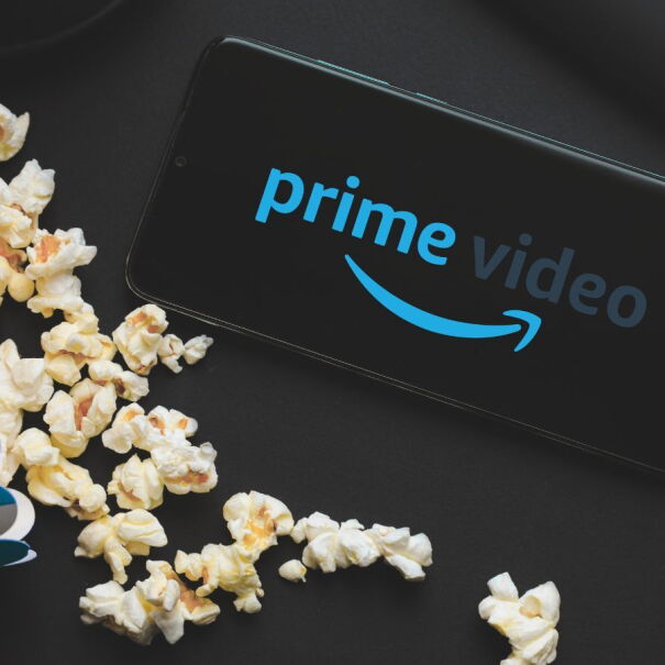 Flatlay of a mobile phone showing the words 'Prime Video' next to a blue-striped tub of popcorn and a pair of earphones.