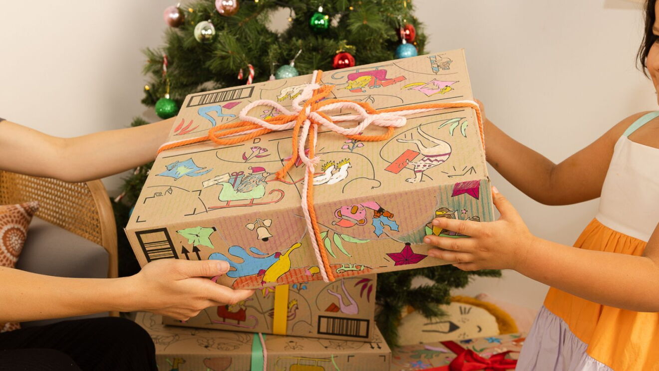 A pair of hands handing a child an Amazon Christmas box.