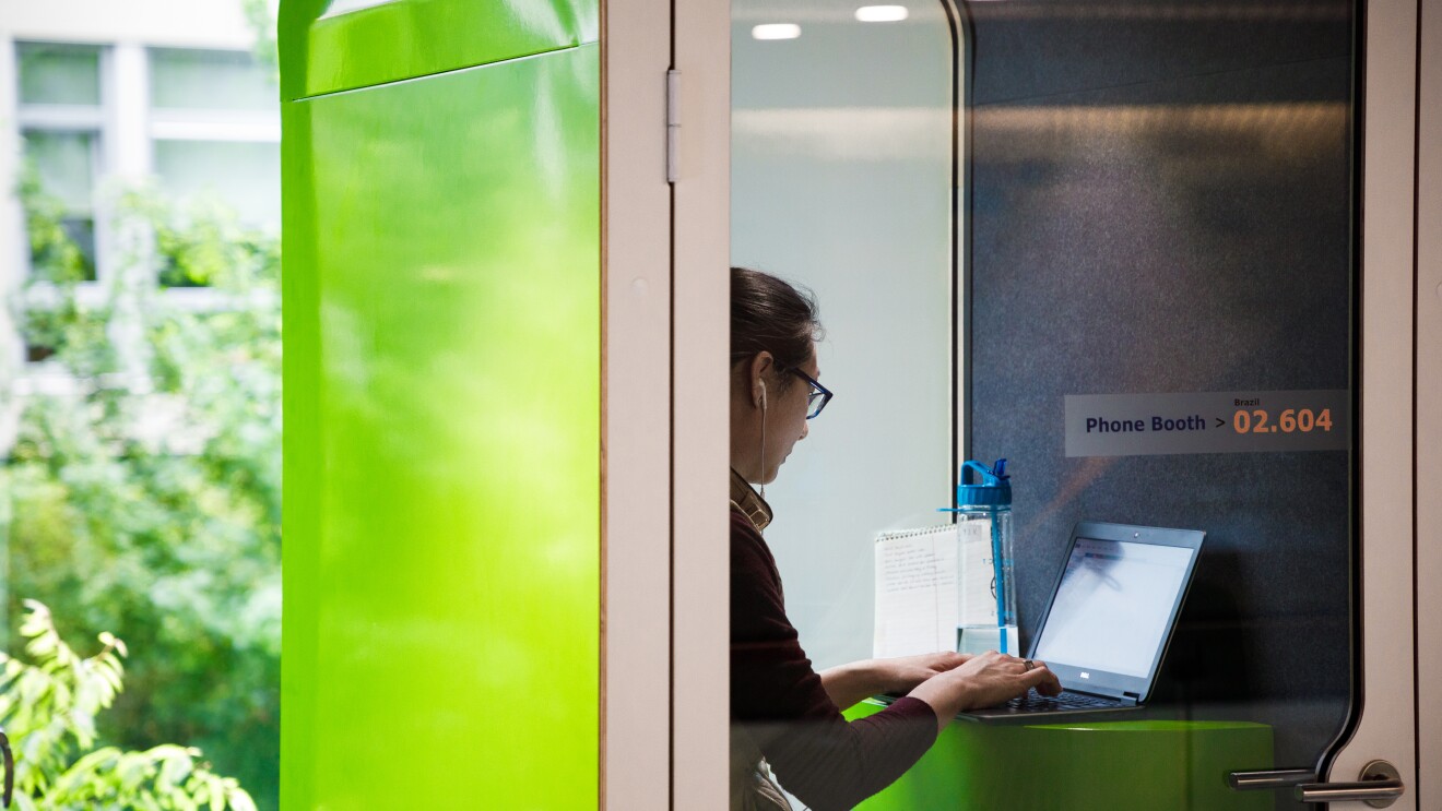 在华盛顿州西雅图亚马逊总部的一个绿色私人电话亭里,一名戴着苹果耳机的女子正在电脑上打字。她桌上放着一个水瓶。