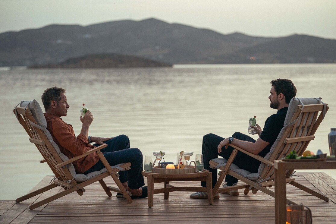 Two men sit by the ocean having a drink