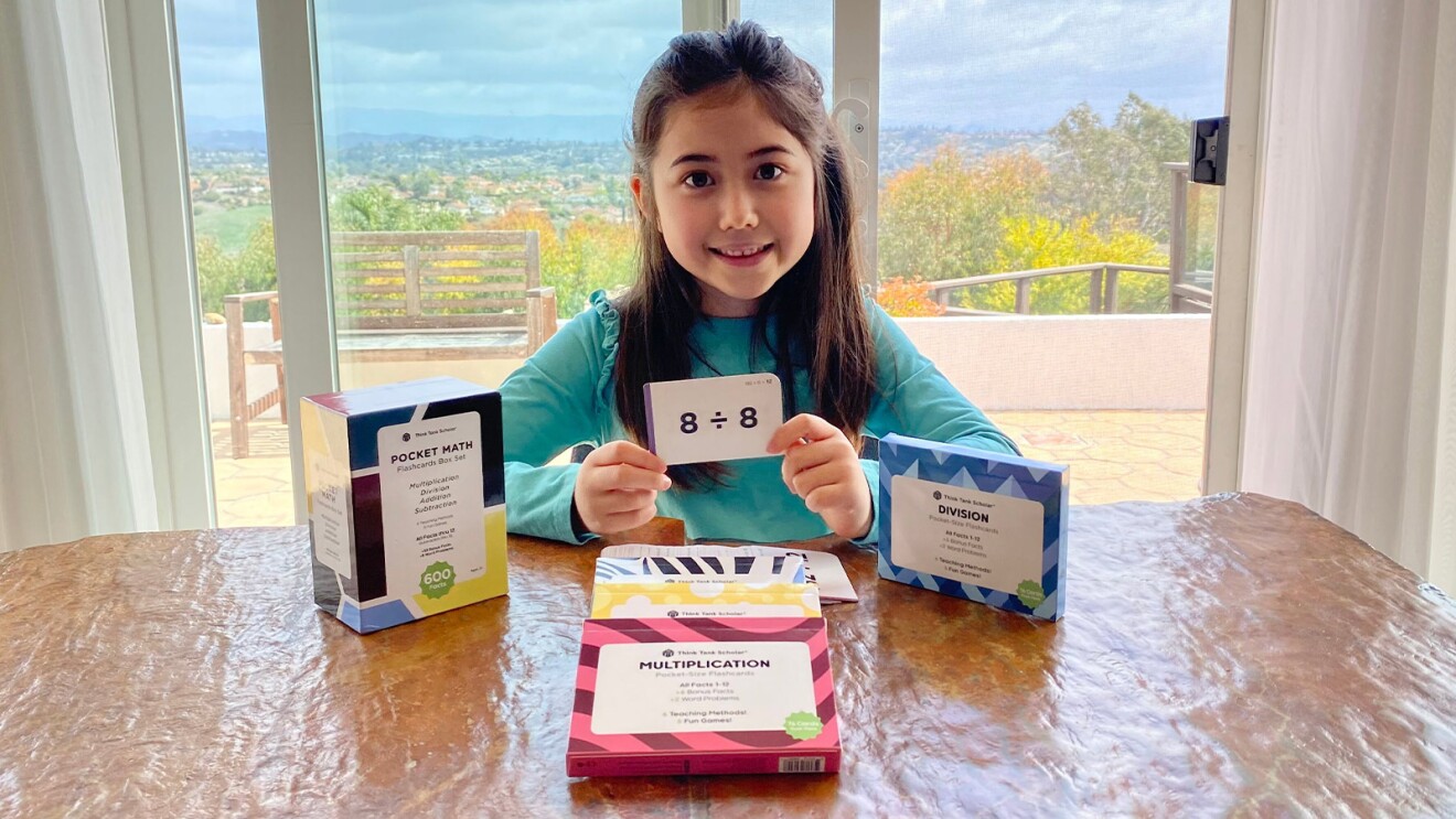 Child proudly displaying math flashcard at table with Think Tank Scholar flashcards