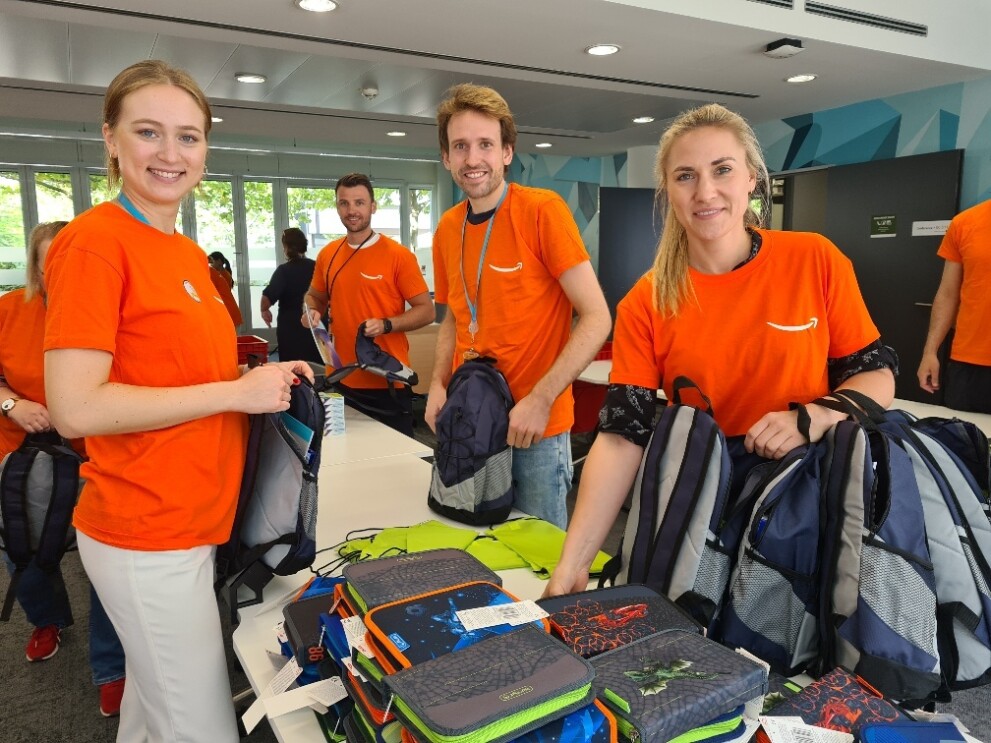 Während der Amazon "Back to School" Aktion packen Amazon Mitarbeiter:innen an einem Packtisch Schuluntensilien für Kinder der Münchner Tafel.
