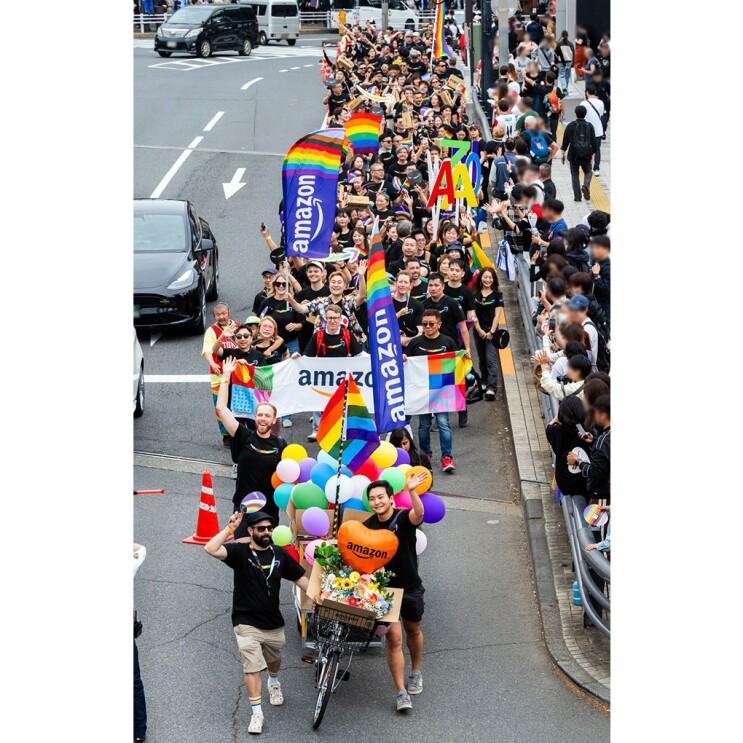 花とバルーンで装飾されたリヤカー付き自転車を先頭にしたパレードの列。彼らの後ろには横断幕などを持つ多数の人が車道を歩いている