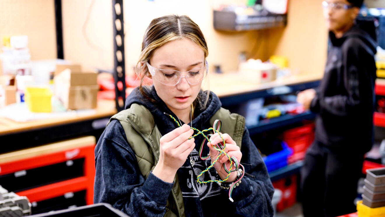 A photo of a student holding wires within a high school robotics classroom.