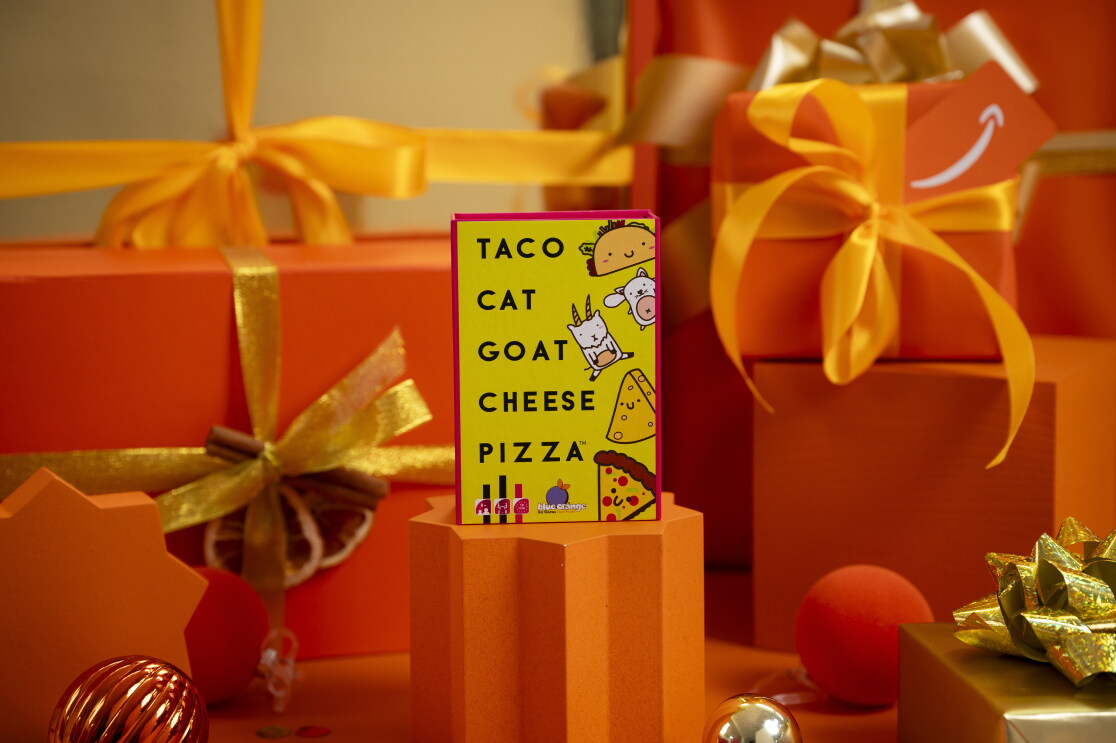The Asmodee Blue Orange Taco Cat Goat Cheese Pizza Card Game surrounded by Christmas packaging 