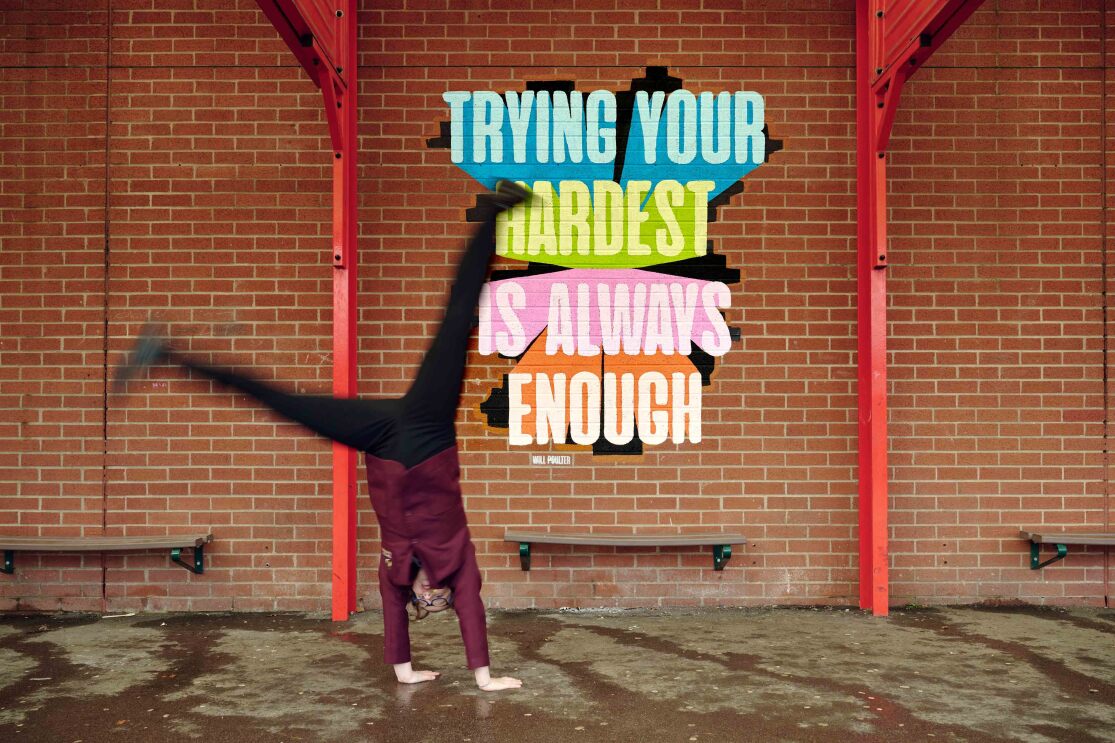 A student does a handstand in front of a Will Poulter quote