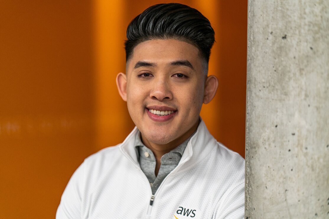 A headshot image of a man smiling for a photo in front of an orange wall.