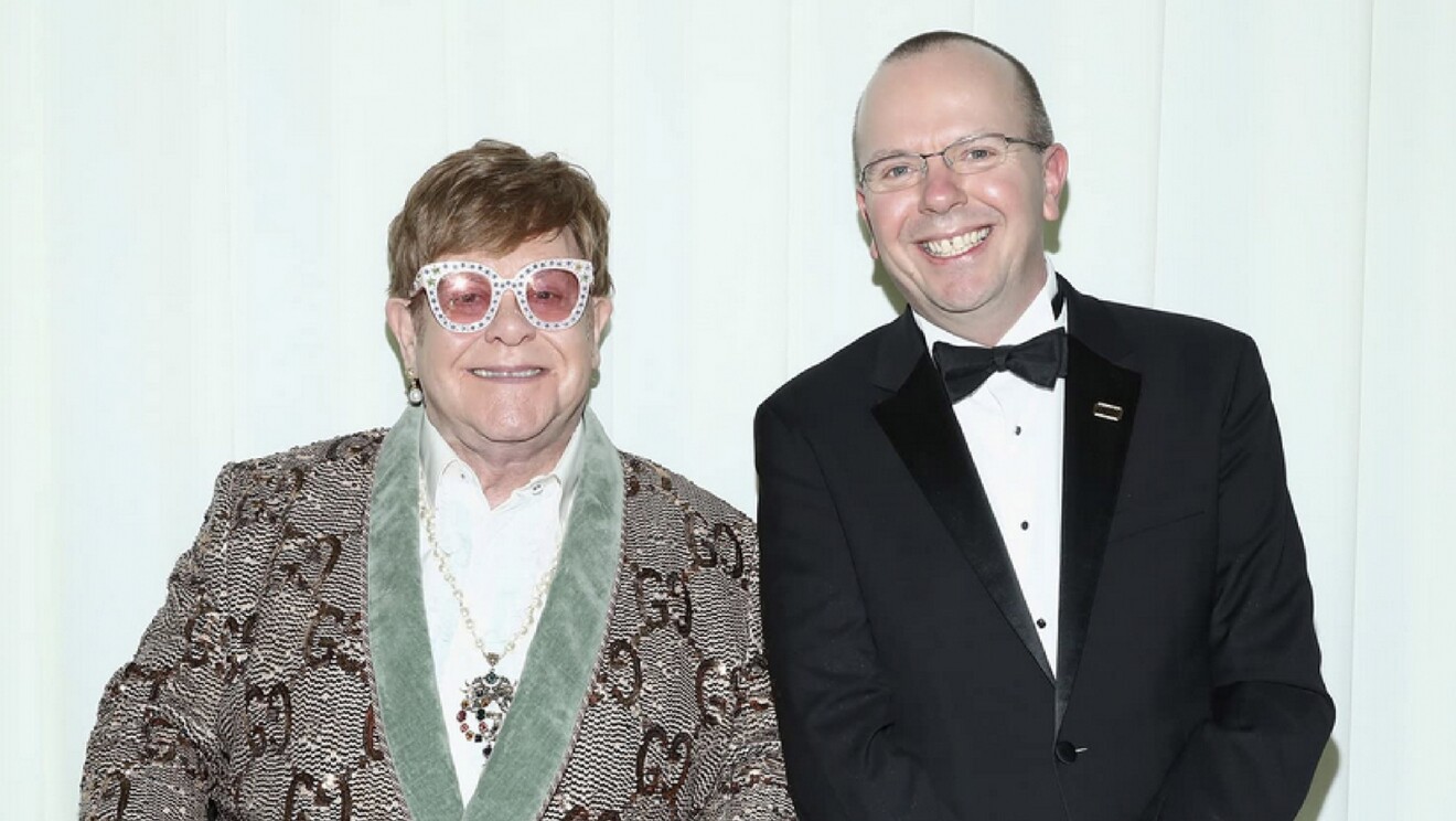 A photo of Col Needham, founder and CEO of IMDb, standing next to Elton John, singer.
