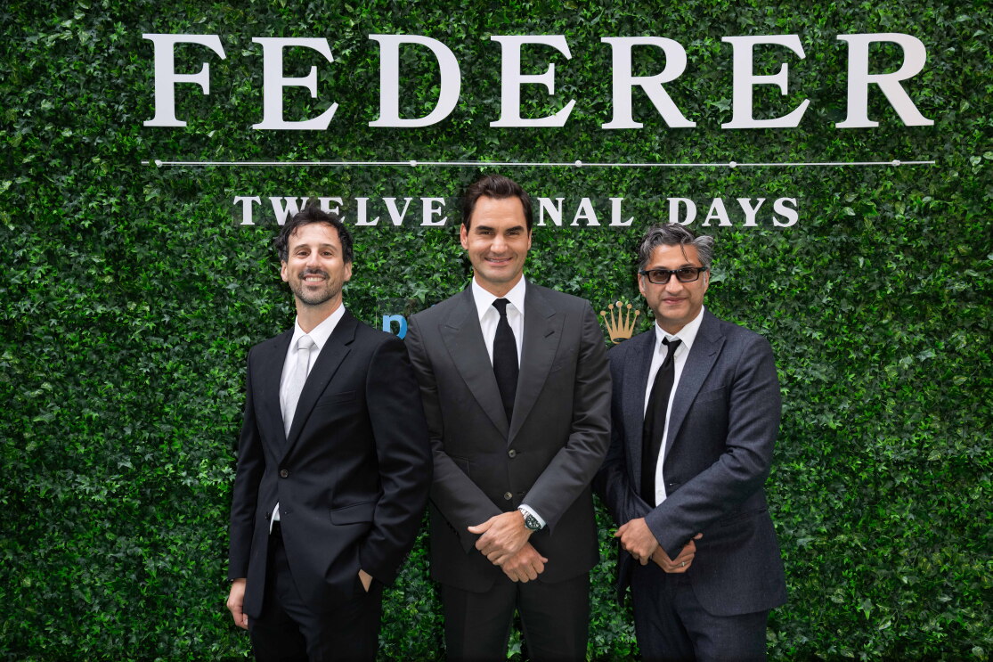Three men in black suits in front of a grass background