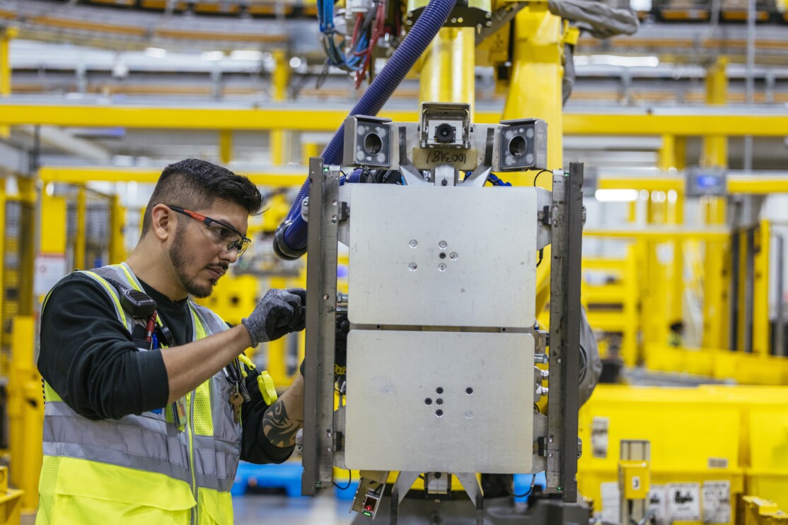 Amazon employee working with robotic machinery in a fulfillment center.