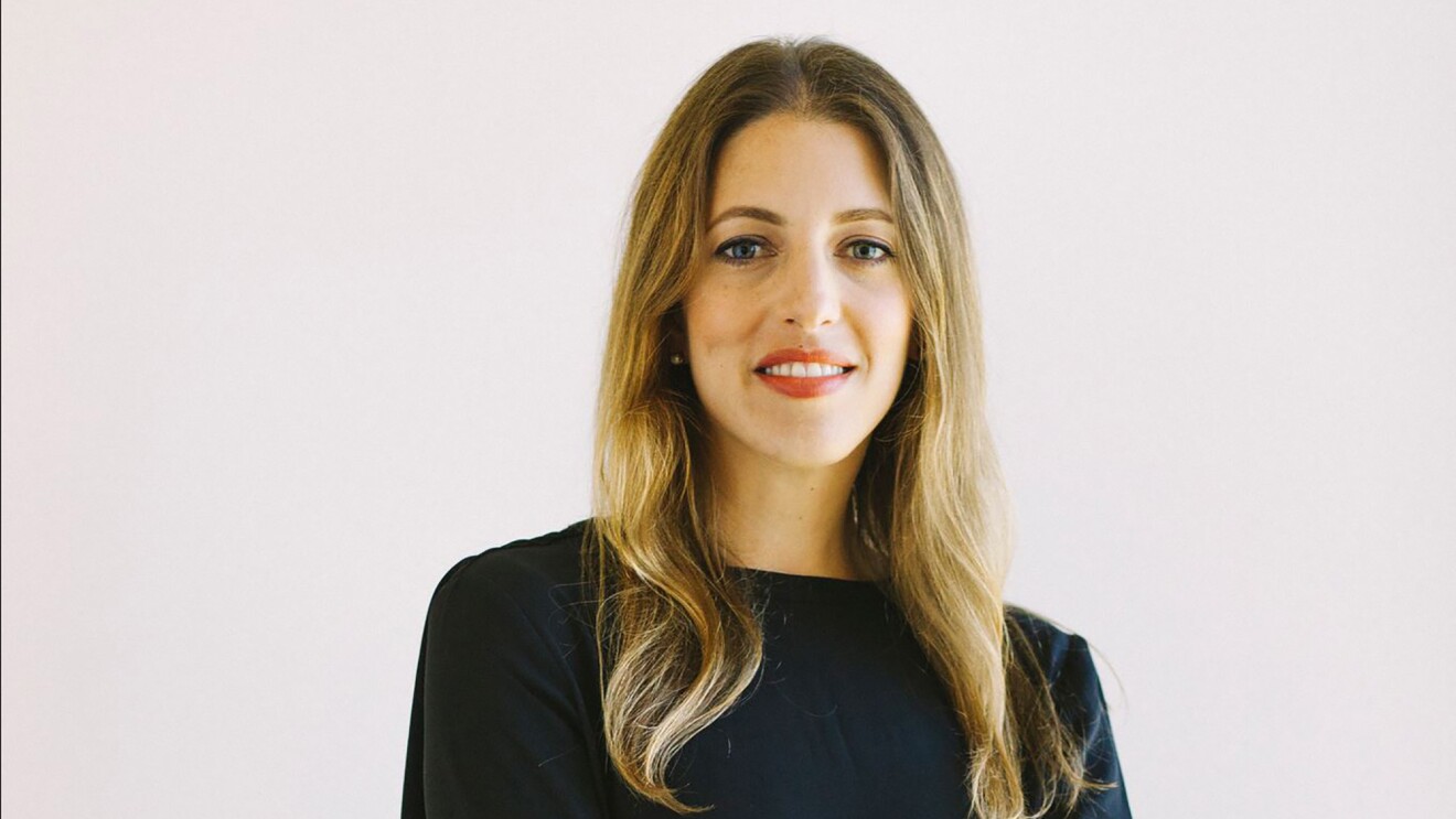 A woman smiles at the camera in front of a neutral background