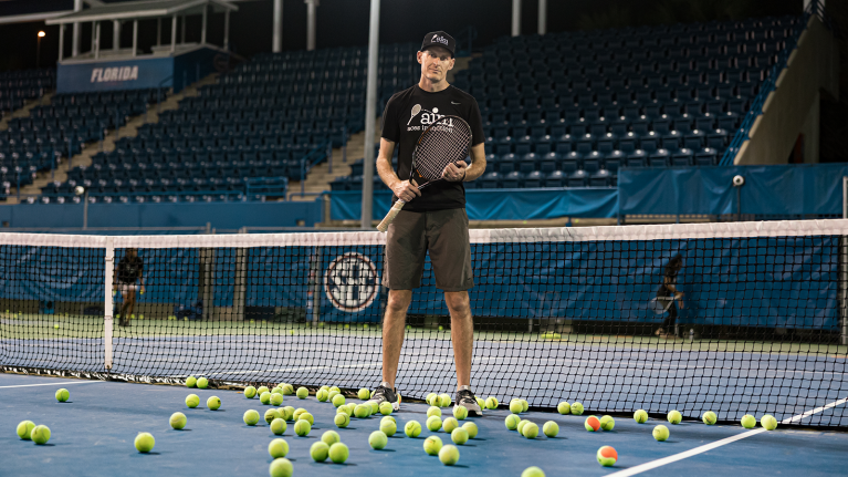 A photo of Addison Staples, program developer of Aces in Motion, standing on a tennis court holding a tennis racket.