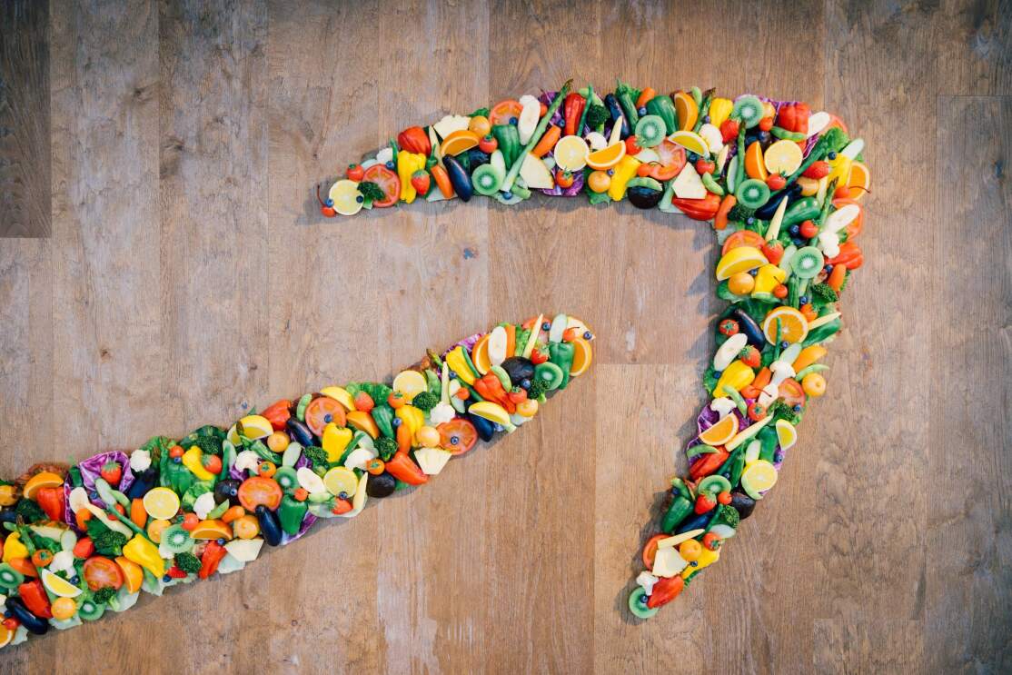 壁に施されたスマイルロゴの矢印部分。プラスチックでできたたくさんの野菜や果物のサンプルを集めて矢印の形をつくっている