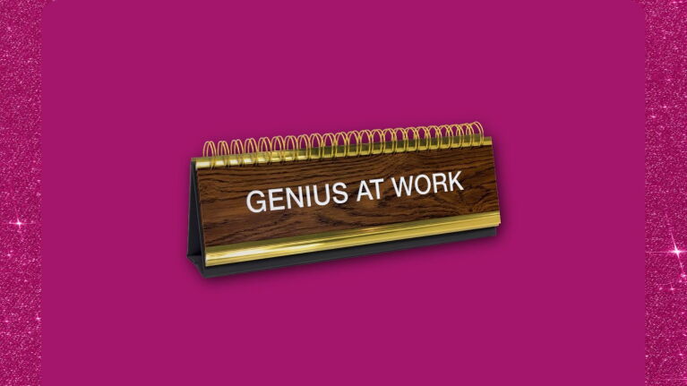 Wooden desk nameplate with 'GENIUS AT WORK' on vibrant pink background