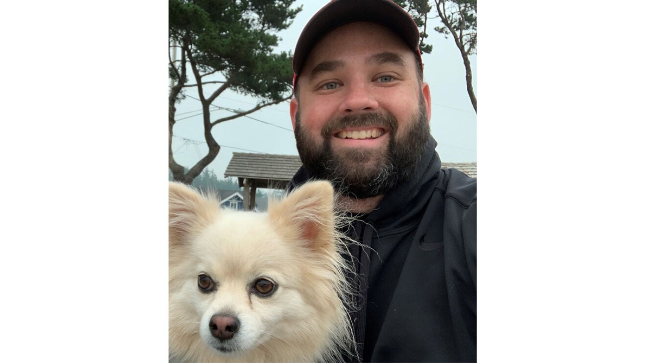An image of a man smiling for a photo outside of his home. It is a selfie photo.