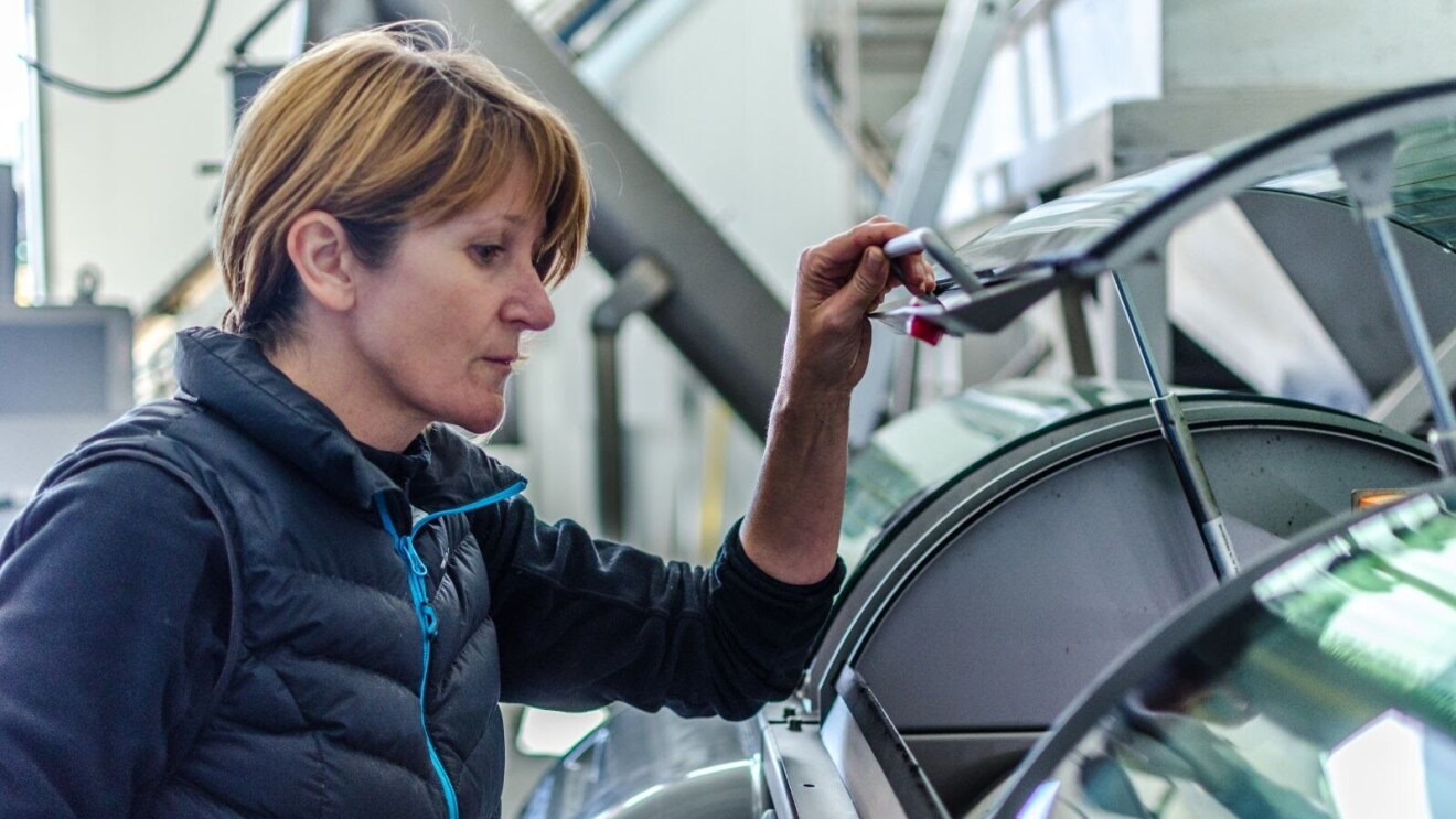 Begoña Gonzalez Pastor, maestra de Almazara y co-fundadora de Olivares de Altomira. La protagonista abriendo una cámara frigorífica de conservación de aceite. Con una mano abre  la puerta de aluminio del frigorífico. La protagonista lleva el pelo corto, rubio y va con un chaleco sin mangas y un jersey negro debajo.
