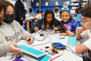 A photo of four students sitting at a table working on tablet devices and keyboards inside the AWS Think Big Space at River Oaks Elementary School.