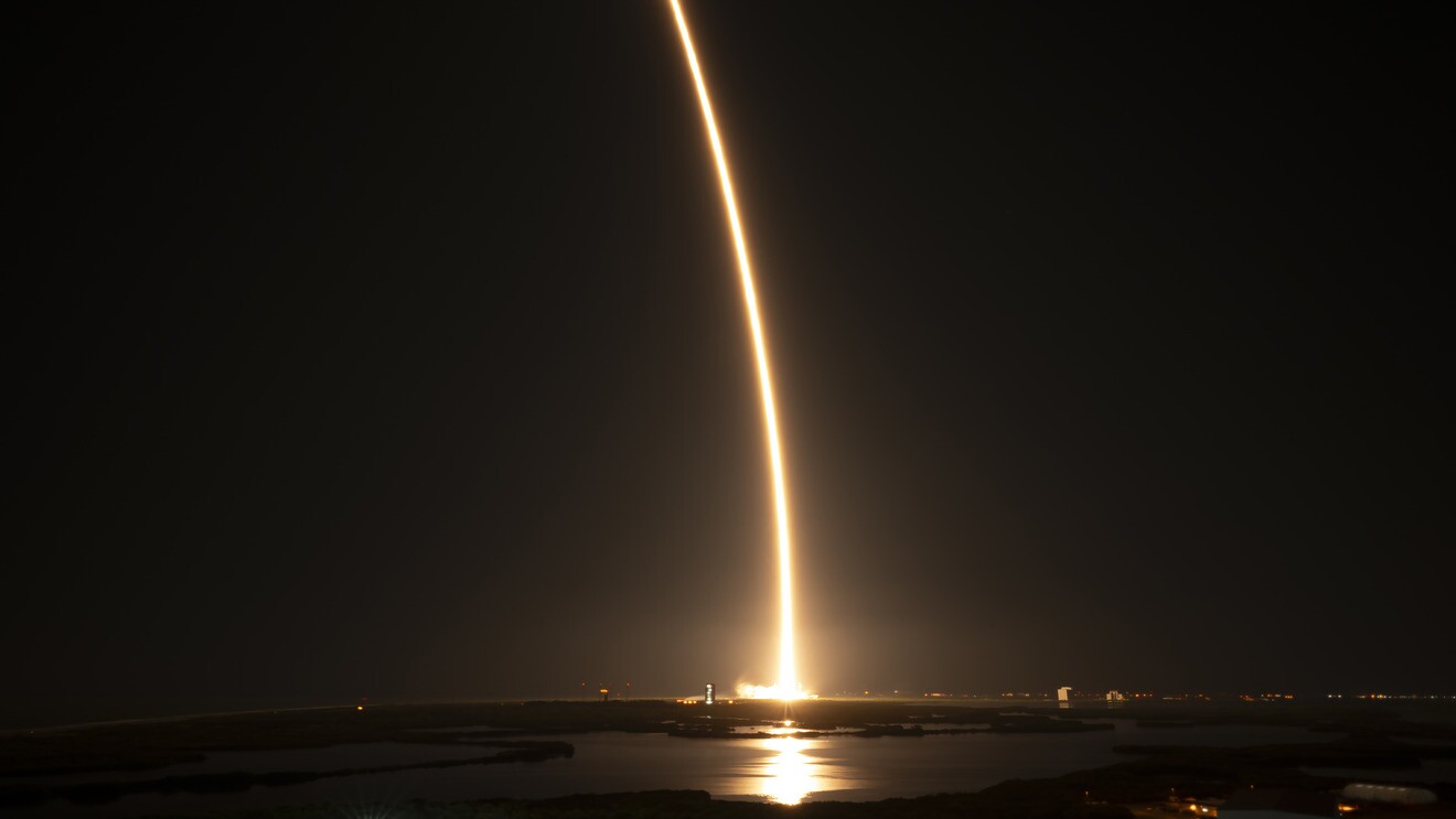 Rocket launch streaking bright light across night sky over water