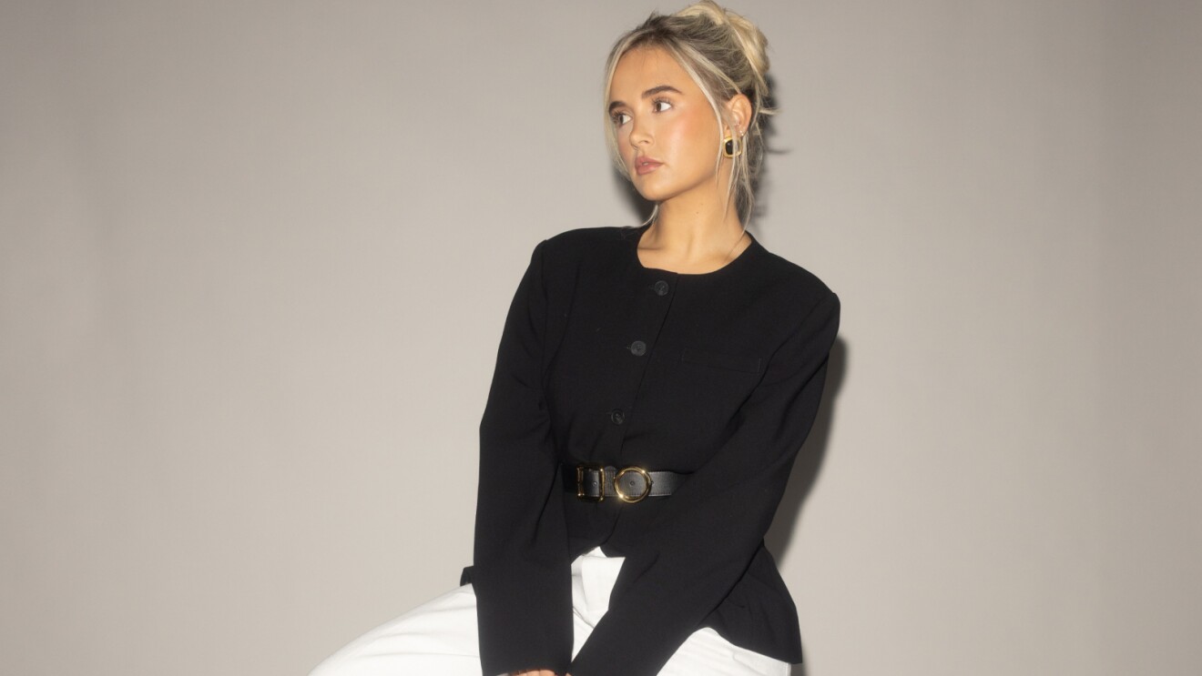 Blonde woman in black top with belt, looking sideways