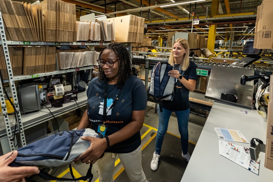 Zwei Logitik Mitarbeiter:innen geben die vorgepackten Rucksäcke weiter.