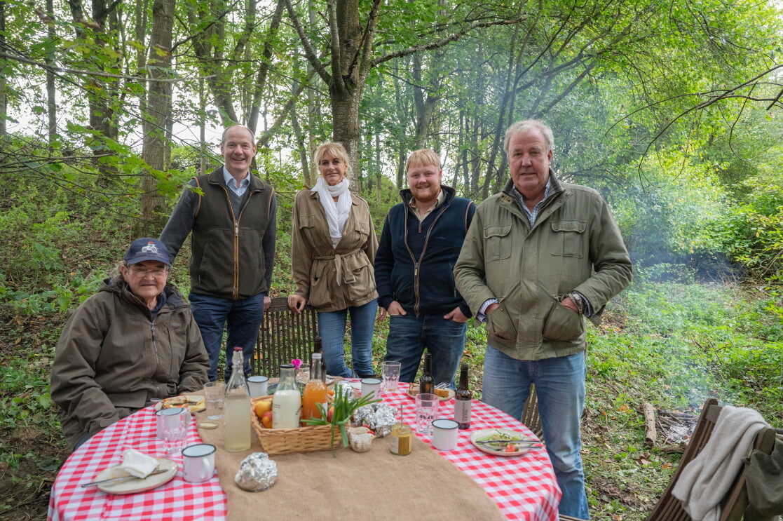 Five people posing for a picture, standing around a table with food and drinks on it