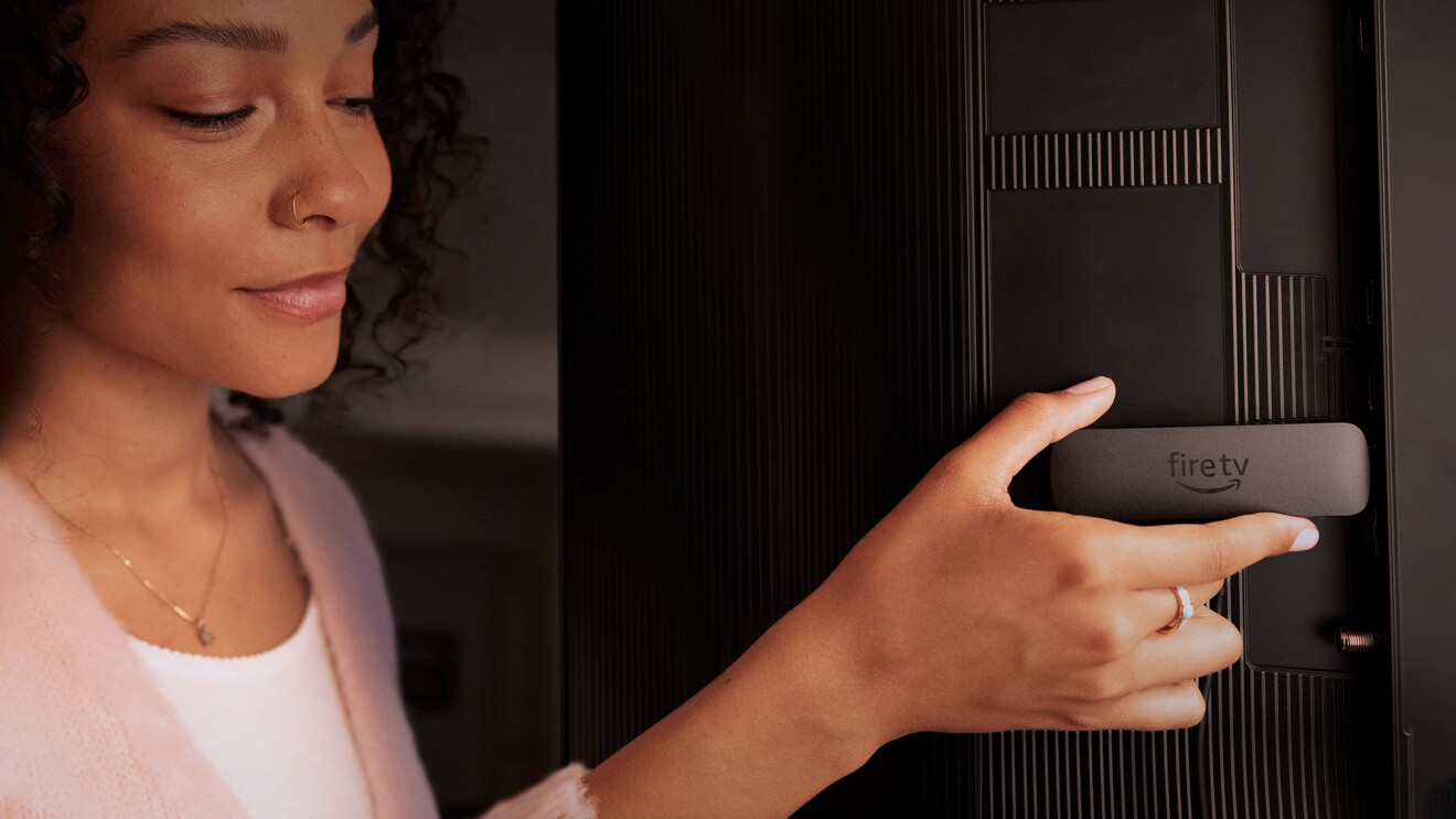 A woman putting a fire tv stick to the back of a TV