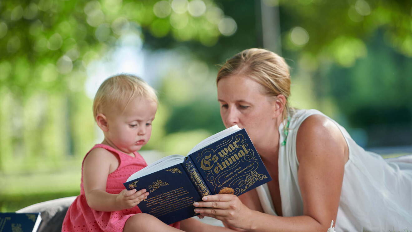 Eine Mutter liest auf einer Picknickdecke ihrem kleinen Kind etwas vor