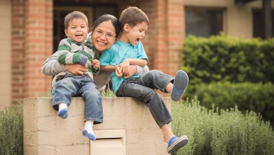 一个母亲的家庭拥抱她的两个儿子,微笑着在他们的家外面拍照。