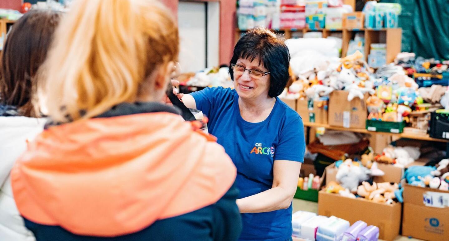 Ukraine Hilfe der Arche in Berlin Community Fund. Mitarbeiterin der Arche verteilt Spielzeugspenden an Kinder. Im Hintergrund sind weitere Kisten mit Spielzeug erkennbar.