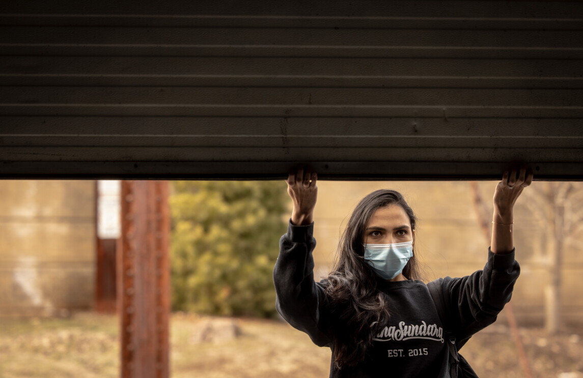 A woman in a mask lifts the door of a warehouse open.