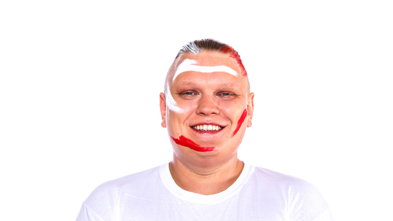 Para el Día de la diversida Amazon ha preparado una acción con asociados de diferentes países que llevan la bandera pitnada en su cara. En la foto, David con camiseta blanca, mirando sonriendo a cámara con la bandera de su país puntada en la cara. Tiene el pelo muy corto marrón y solo en la parte superior. En los laterales lo lleva completamente rapado. 