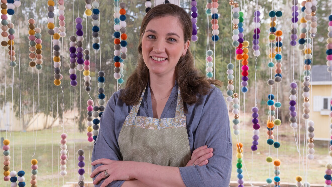 Amazon Handmade seller posing in a photograph in front of the felted wool ball garlands she makes and sells.