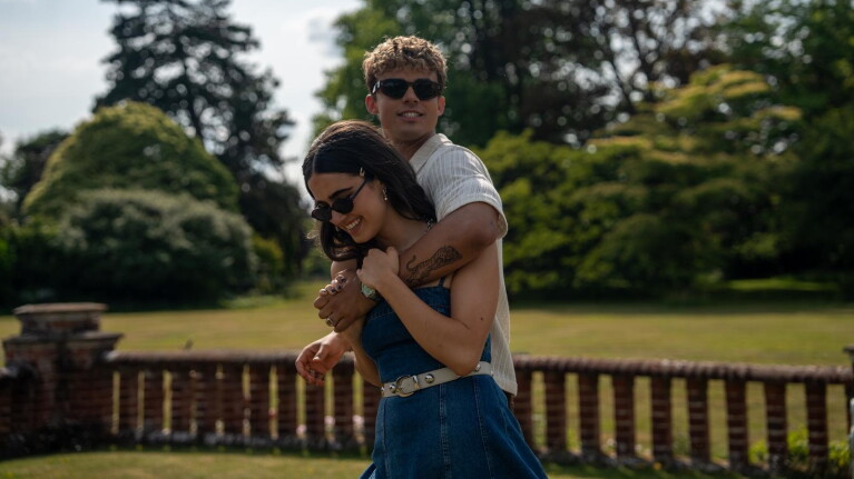 Young couple walk arm in arm smiling with a countryside background