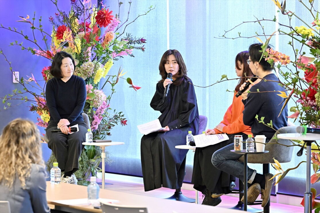 ステージでの話者たちが左から2番目の女性話者の話を聞いている。