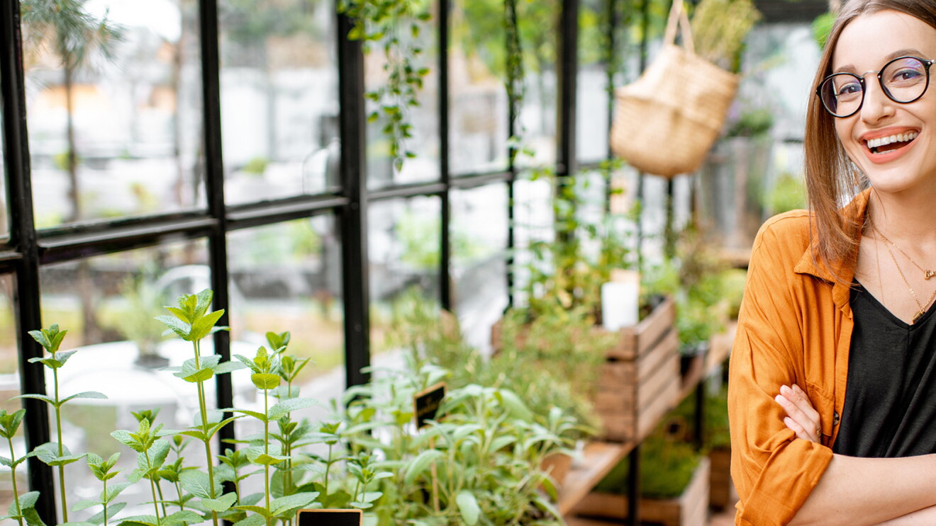A woman smiles from inside a green house, her arms crossed.