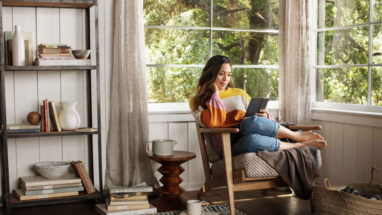 A girls reads on her Kindle from the comfort on her home snuggled on a chair by the window