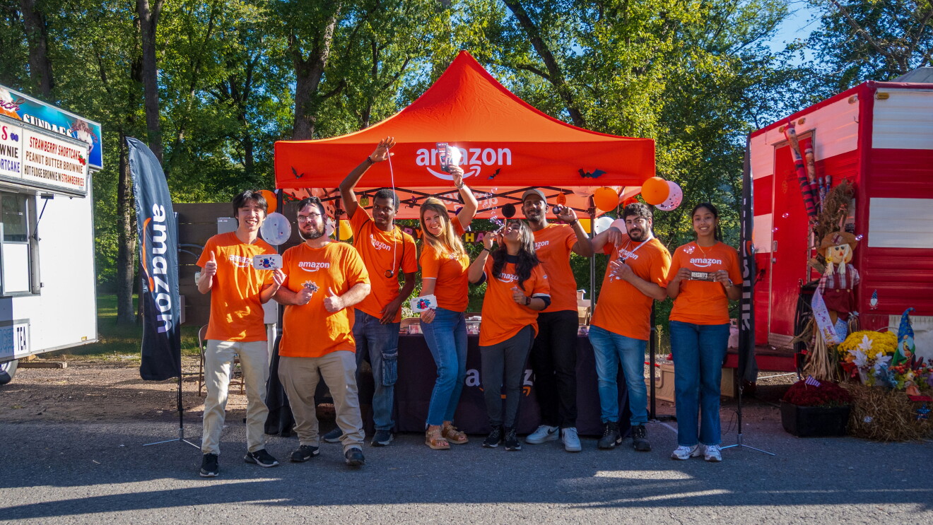 Amazon community volunteers under an amazon orange volunteer tent posing at a community event