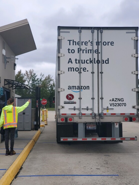 An Amazon employee in safety gear and mask gives a "thumbs up" to an Amazon truck as it drives off, full of customer orders.