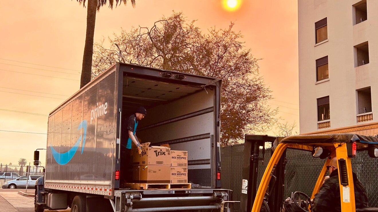 Amazon delivery employee handling boxed of donations in Prime truck against an orange sky