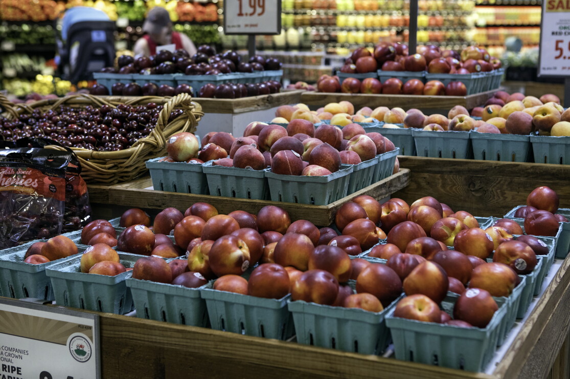 Produce displayed in a Whole Foods Market store - nectarines, cherries, and peaches are in the foreground, with a refrigerated juice display behind it. 