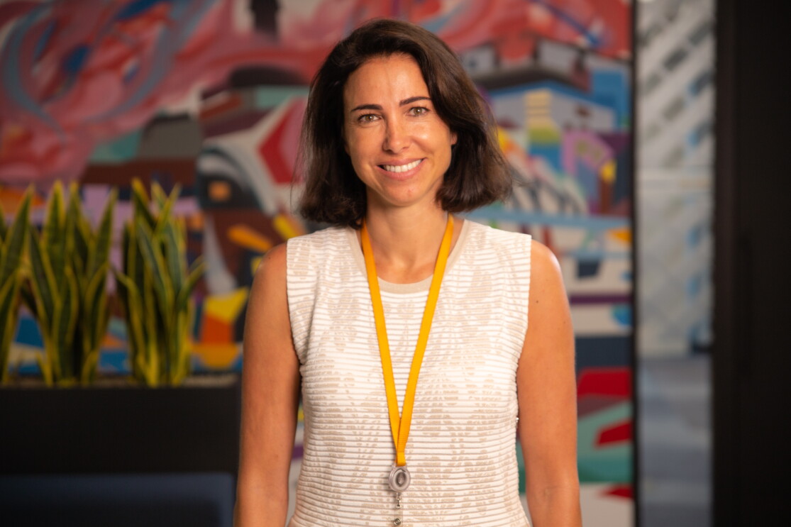 Ruth Díaz, Vicepresidenta de Amazon Fashion en Europa. En las oficinas corporativas de Amazon en Madrid, Ruth aparece en un plano hasta la cintura. Llev amedia melena morena, un jersey blanco con dibujos de flores en beis. Lleva la tarjeta de Amazon en una cadena amarilla de ropa. Con los ojos azules, mira a cámara con una sonrisa. 