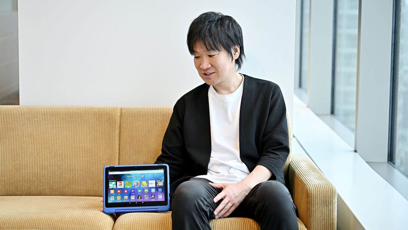 座っている男性がソファに置かれているタブレットを見ている。