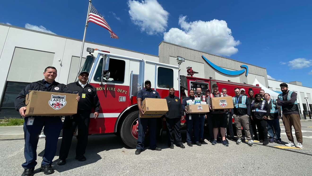 Firefighters and Amazon employees standing in front of a fire truck parked by an Amazon fulfillment center