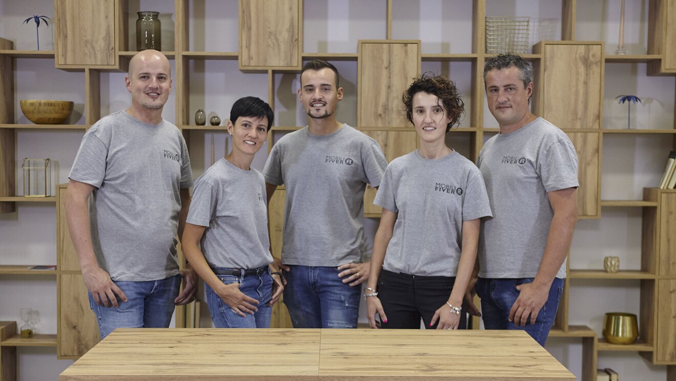 I fratteli Gobbo in posa davanti ad un tavolo Fiver. Sono 2 donne e 3 uomini, indossano t-shirt grigie e jeans