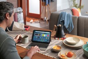 looking over a man's shoulder as he sits at a dining table covered in plates, a kettle, and table runner. he is browsing his fire max 11 tablet with a keyboard accessory