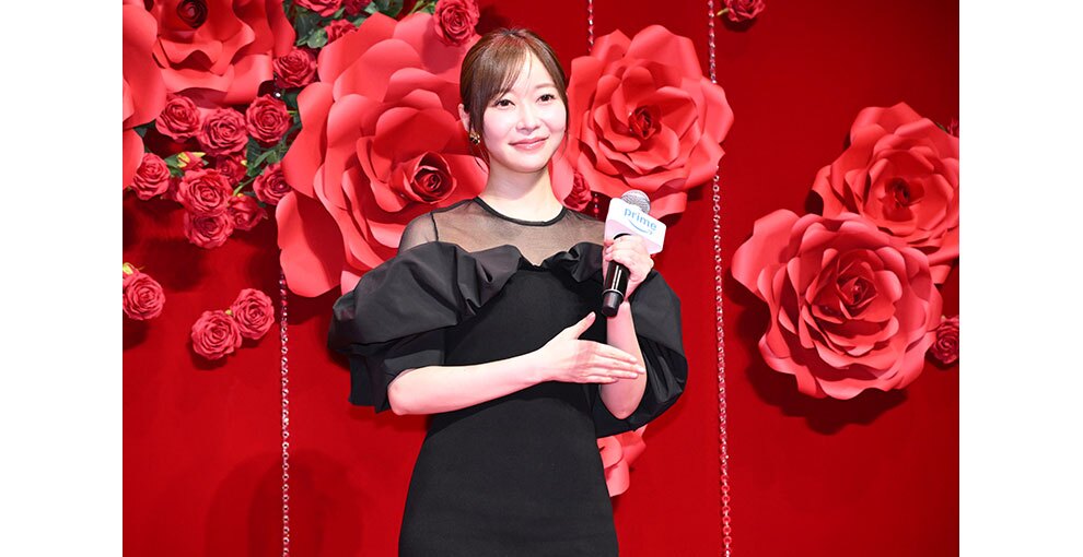 赤いバラの花の大きなオブジェと生花の赤いバラが飾られた赤い壁を背に、マイクを持ったドレス姿の女性。